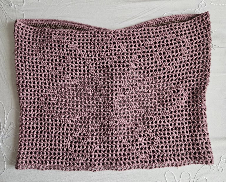 Handmade mauve crochet tube top with a mesh stitch pattern laying flat on a white floral fabric.