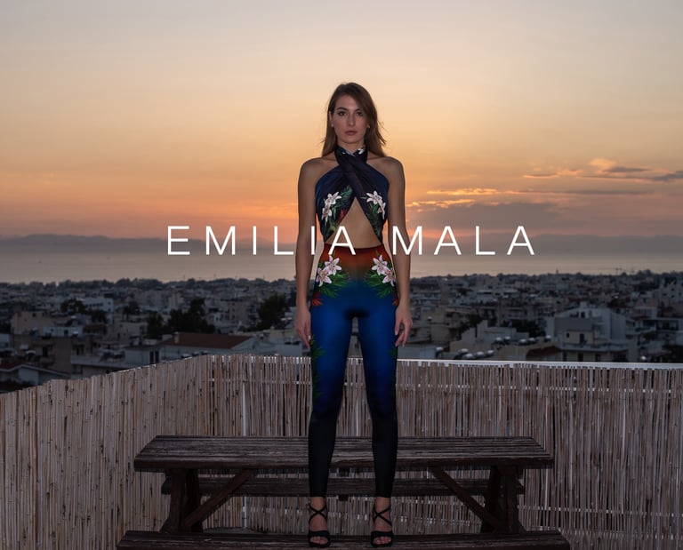 Model in Emilia Mala floral printed jumpsuit on a rooftop at sunset overlooking a city skyline.