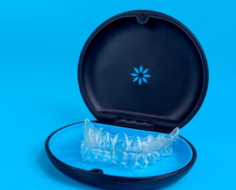 Clear teeth aligners inside a black protective carrying case on a vibrant blue background.
