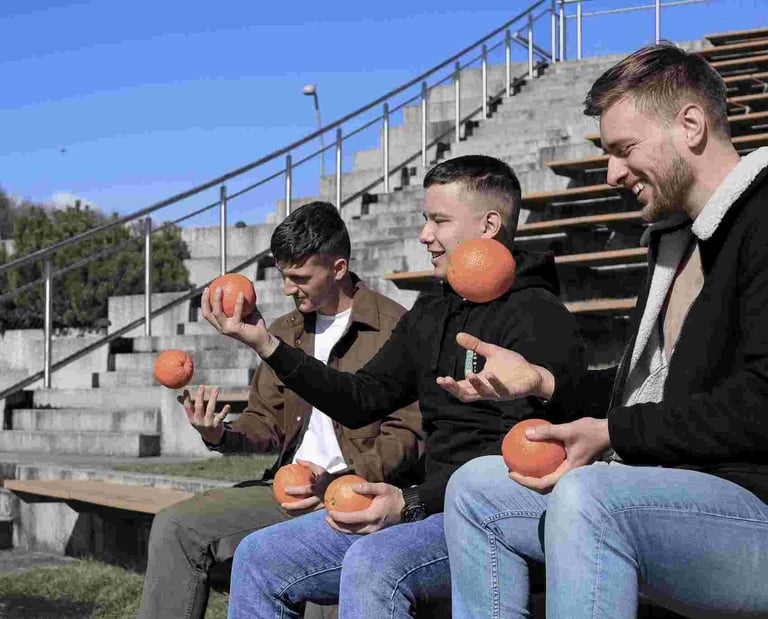 Trys jauni vyrai sedi ir meto apelsinus