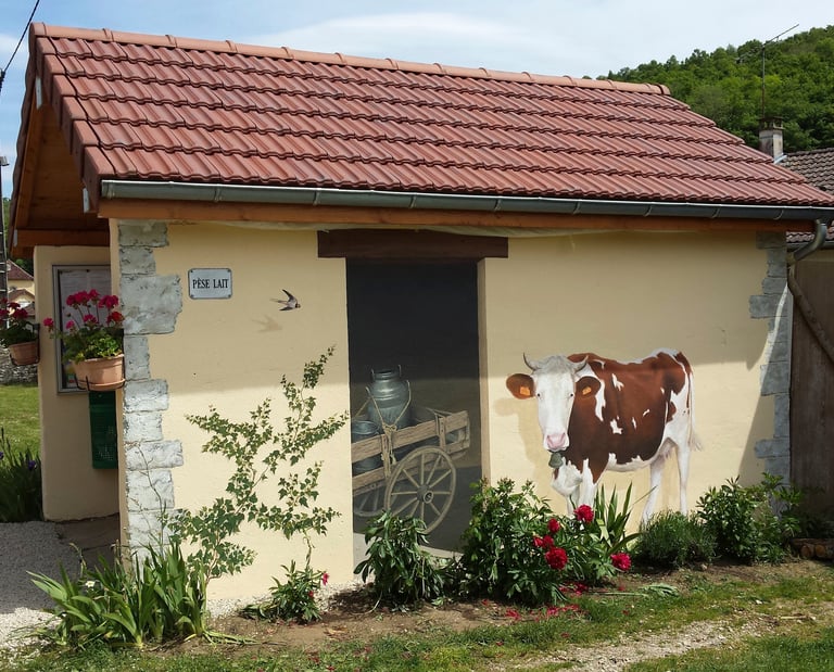Fresque murale sur façade comporte une fausse porte, une vache et un lierre peints.