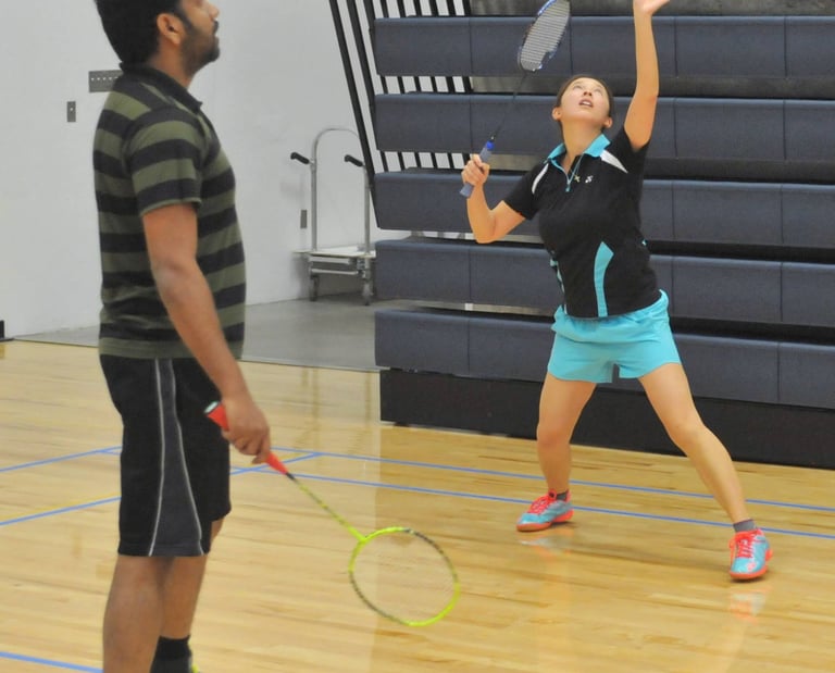 Ellen  preparing to serve during a badminton match in an indoor gym.