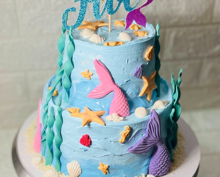 Two-tier light blue mermaid birthday cake for a fifth birthday decorated with shells and tails.