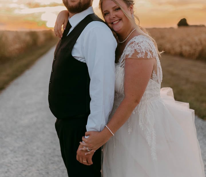 a bride and groom standing in front of a sunset