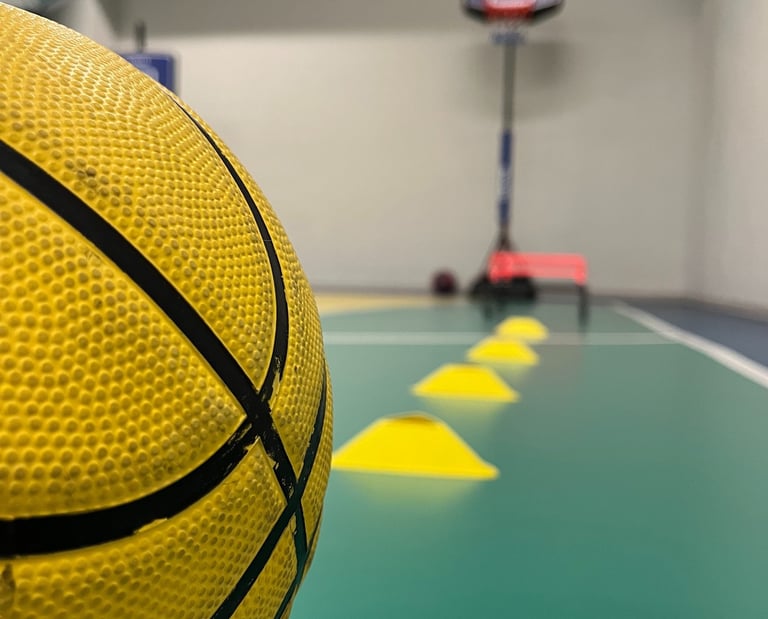 Primo piano di un pallone da basket giallo in un'area multisport della palestra Move 2 Grow a Milano, con coni e canestro sul
