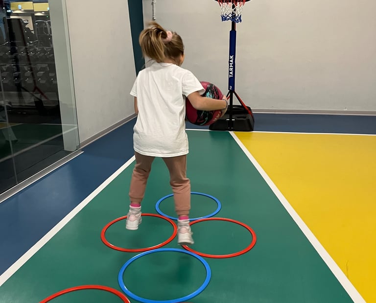Bambina che gioca con un pallone su un campo multisport nella palestra Move 2 Grow a Milano, utilizzando cerchi colorati 