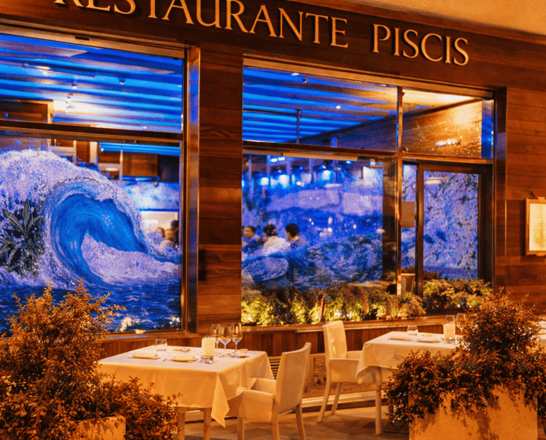 Elegant outdoor dining at Restaurante Piscis with wave murals and set white tables.
