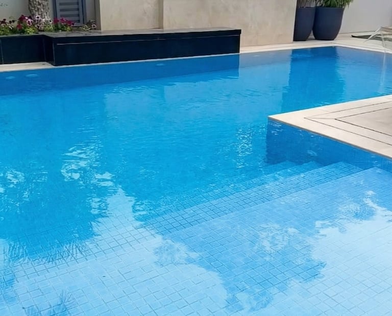 Luxury backyard swimming pool with blue tiles, stone water feature, and tropical landscaping.