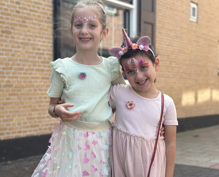 Twee meisjes die vrolijk poseren met roze bloemen- en eenhoornschmink.