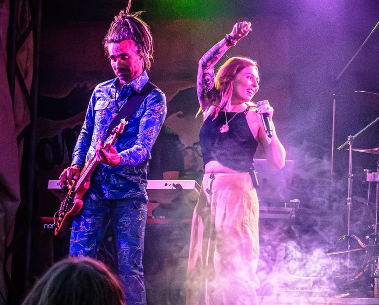Live band performing on stage with a female singer and bass guitarist under purple and green stage lights.