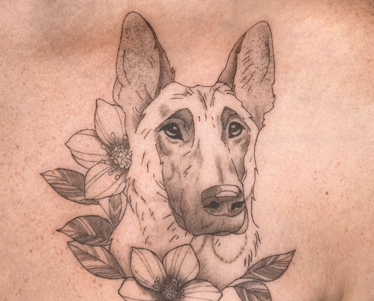 Tatouage en fine line d'un chien malinois entourée de fleurs sous la clavicule
