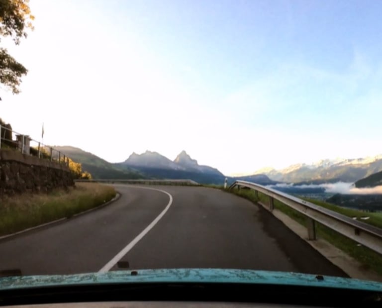 Winding mountain road with a view of the Swiss Alps during a scenic summer car drive.
