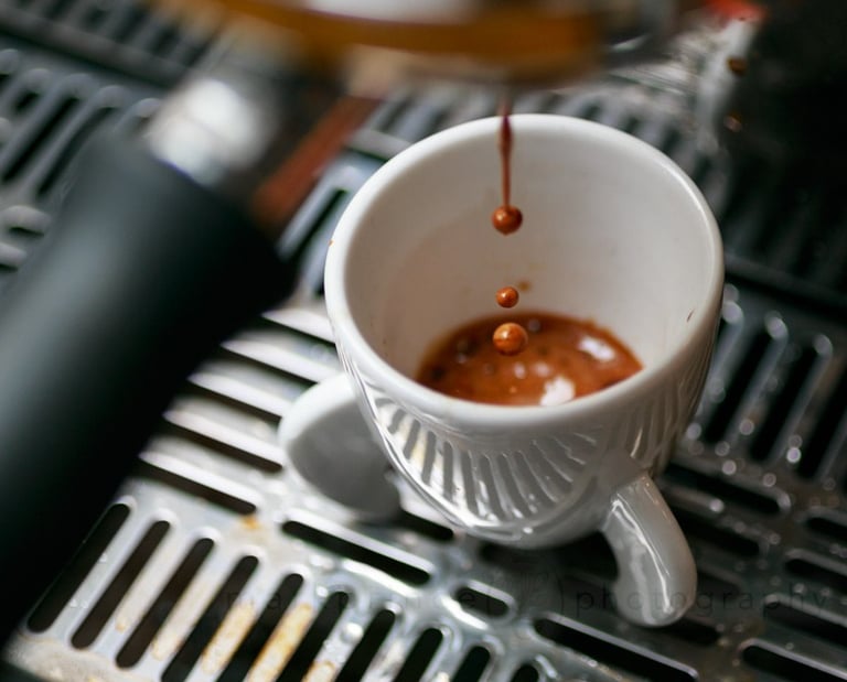 Fresh espresso dripping from a professional coffee machine into a white ceramic cup.