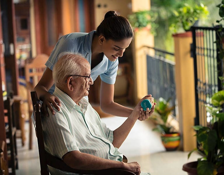 A female home care nurse assists an elderly man with dumbbell physical therapy exercises outdoors.