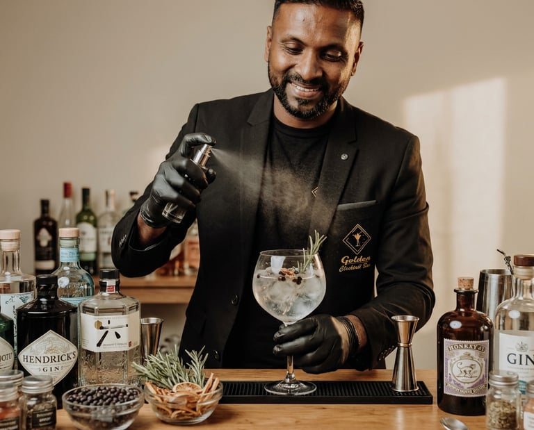 Professional bartender spraying botanical mist onto a gin and tonic cocktail with aromatic garnishes.