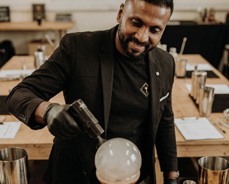 Professional mixologist using a torch to create a smoke bubble on a craft cocktail at a bar event.