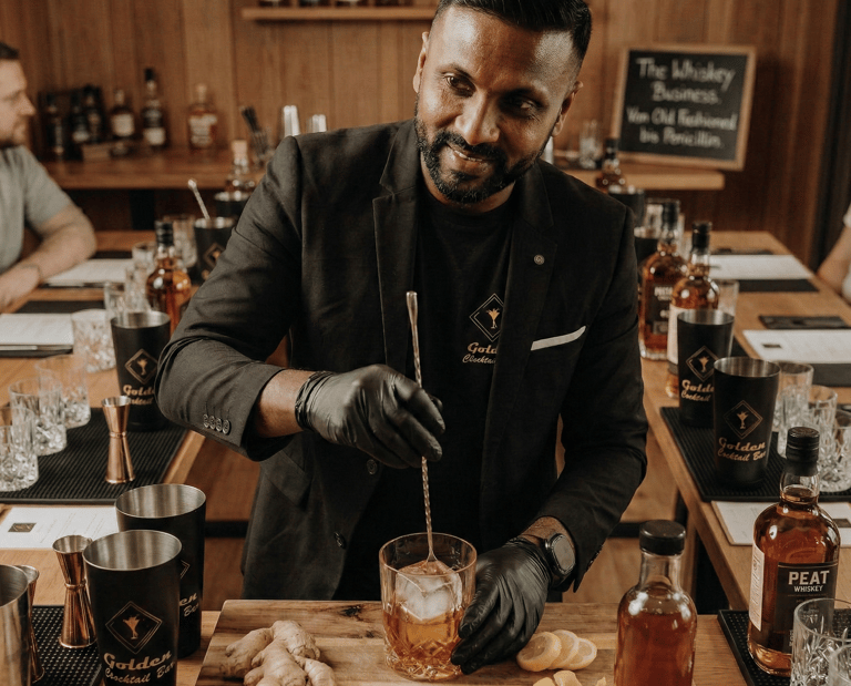 Professional bartender in a black suit mixing an Old Fashioned whiskey cocktail at a tasting event.