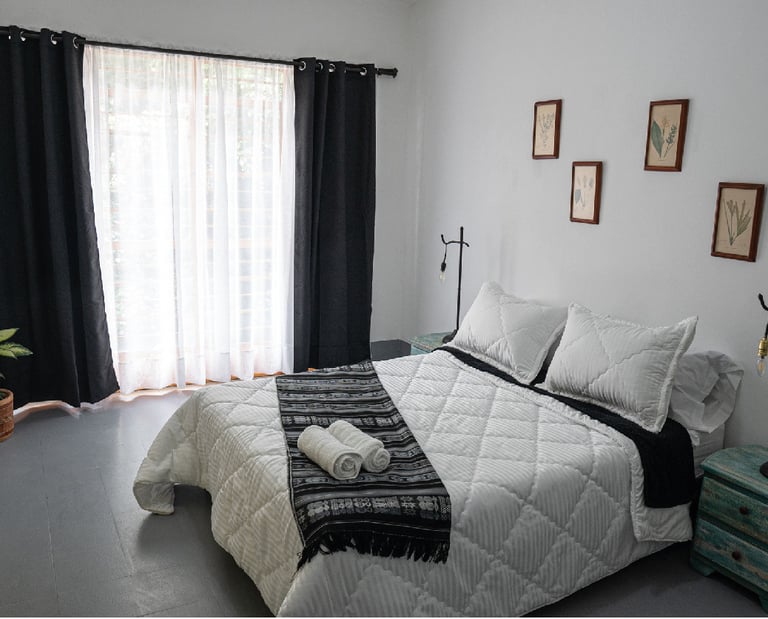 Modern guest bedroom with a white quilted bed, black curtains, and rustic wooden nightstands.