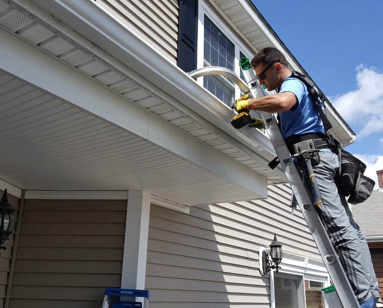 Technician safely positioned on a ladder tightening a heavy-duty gutter bracket with a drill, reside