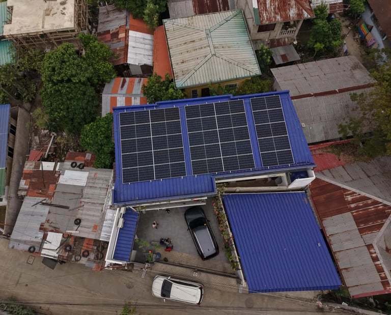 An aerial drone shot of a residential house with a bright blue metal roof featuring a large array of black solar panels