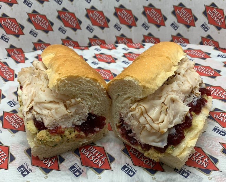 A sliced turkey cranberry sub sandwich with stuffing on a hoagie roll with deli branding.