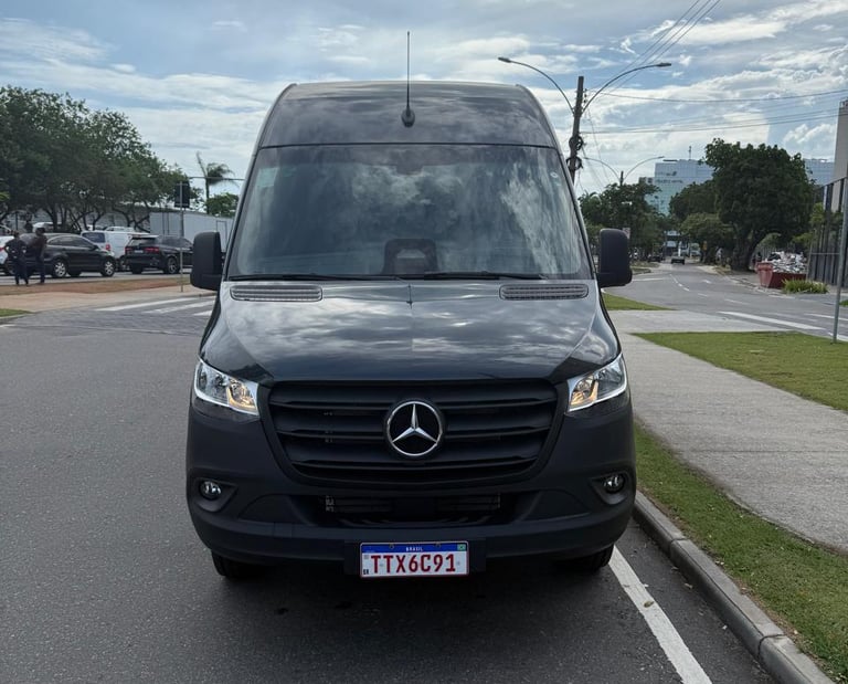 Front view of a black Mercedes-Benz Sprinter van parked on a city street under a cloudy sky.