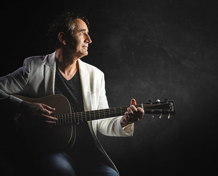 Joël Royer en photo avec sa guitare et de profil avec un fond noir