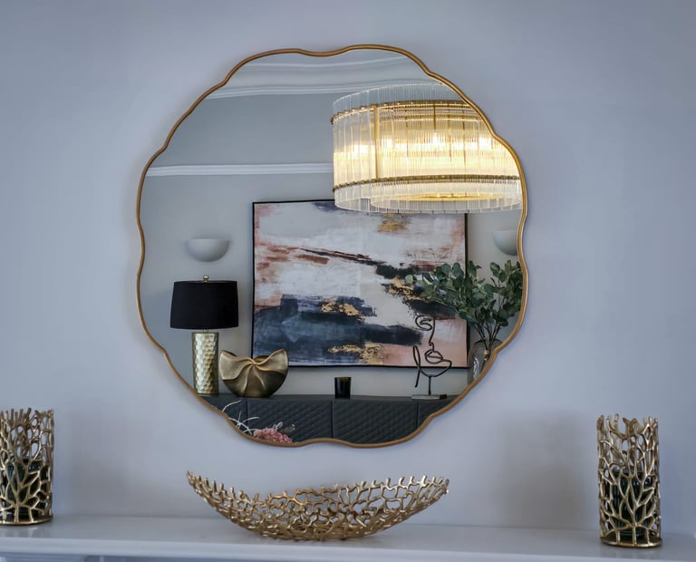 Gold-framed mirror reflecting modern decor with chandelier, abstract art, and stylish accents