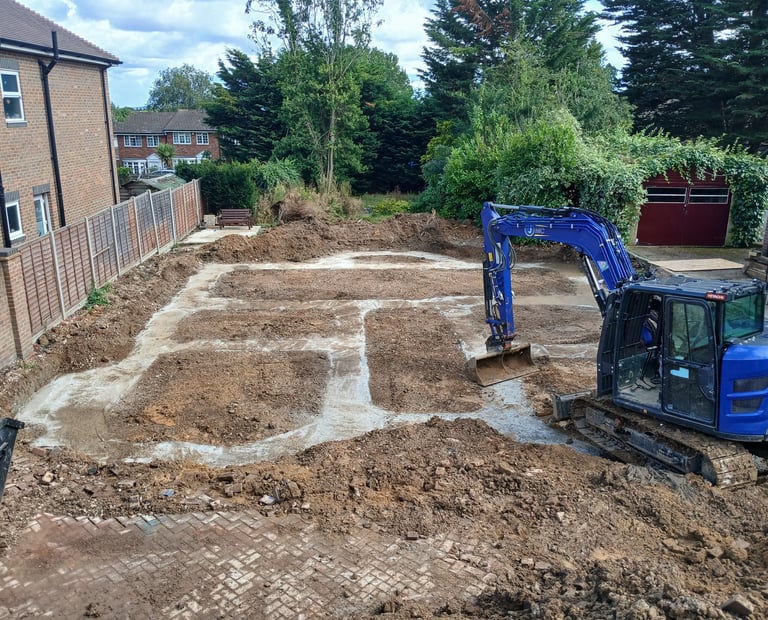 Blue excavator digging concrete footings for a new house foundation in a residential construction site.