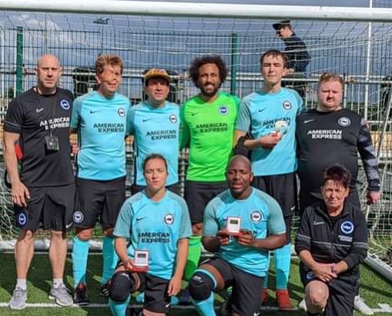 Group photo of a football team and staff standing in front of a goal on an artificial pitch.
