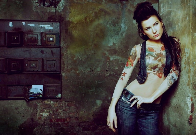 Audrius Turskas photography a woman with tattoos on her chest standing next to old textured wall