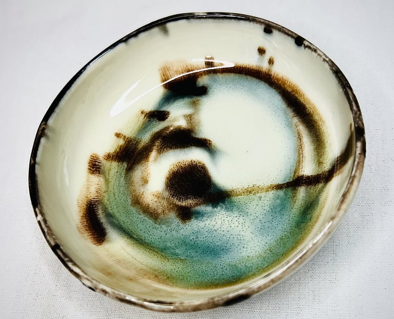 A glazed plate with black lid and abstract brown and green spots and shades