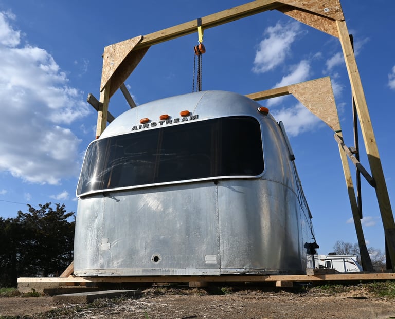 Shell of Airstream on the ground, two large gantry crane holding shell in place.