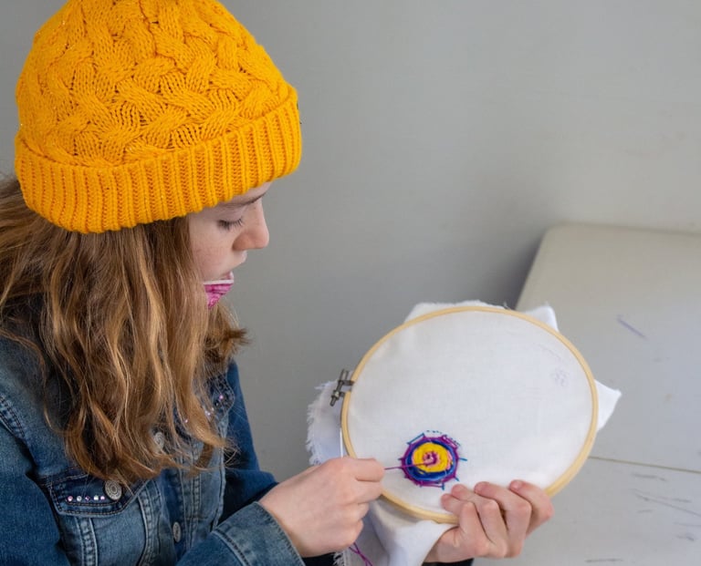 Young girl pulling thread through fabric to create an embroidered spider web.
