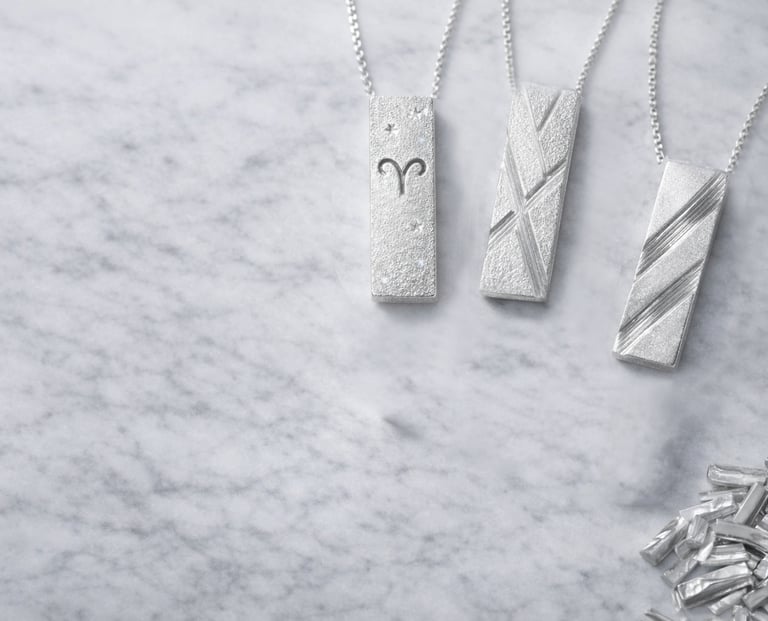 Minimalist silver pendants displayed on marble, highlighting clean lines and texture