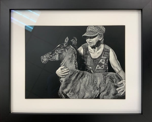Detailed scratchboard art of a woman hugging a newborn foal in a black frame.