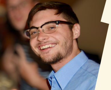Smiling young man with a beard and glasses wearing a blue dress shirt.