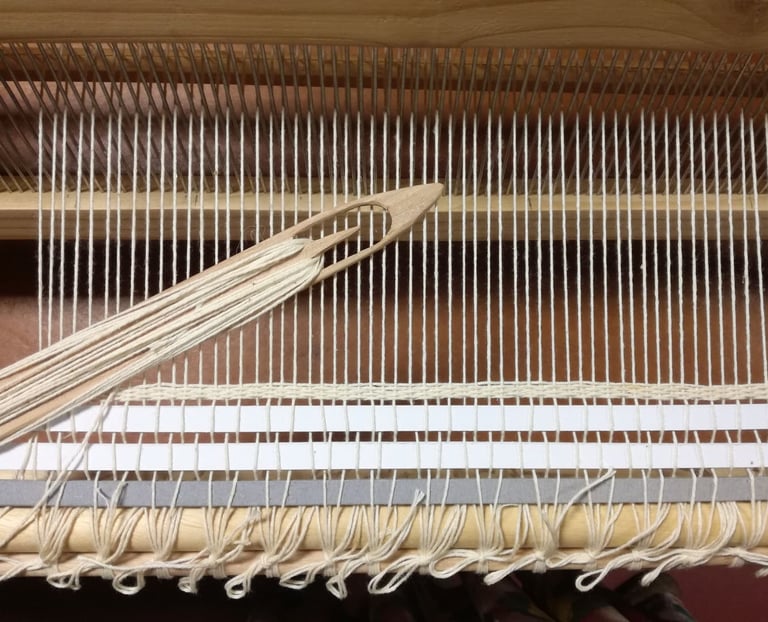 a weaving loom with a white cotton warp and a wooden shuttle with white cotton thread