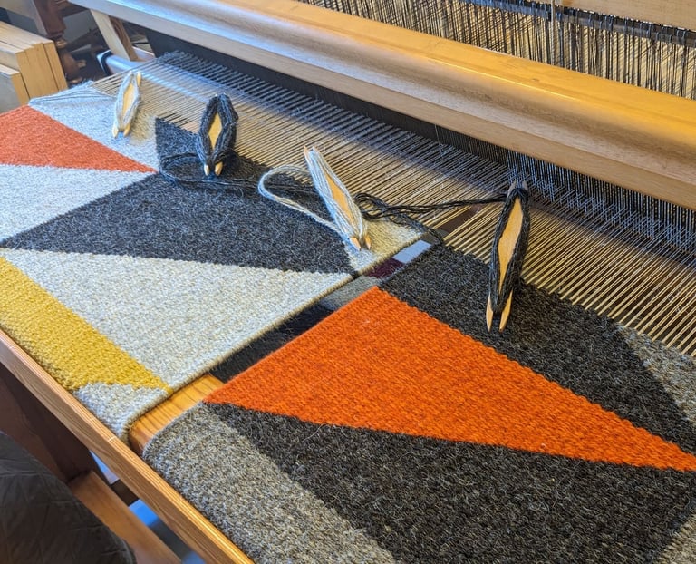 a weaving loom with shuttles and gray orange yellow black wool threads on a kilim rug in progress