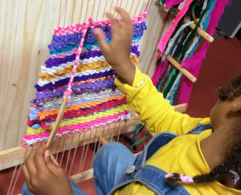 a young girl sits on a chair and weaves colorful rag rug on a weaving loom
