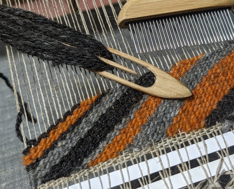 a weaving loom with shuttle, combe and black grey orange wool diagonal threads on a navajo rug in pr