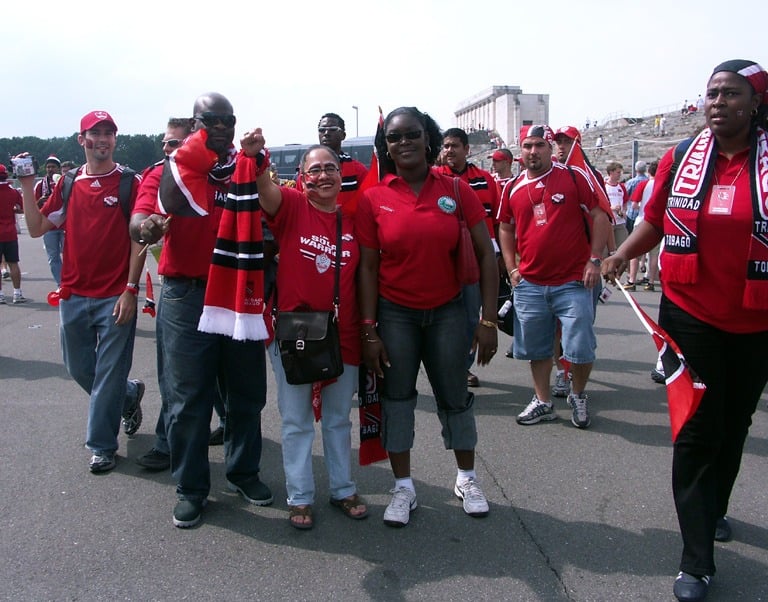 Crowd of Soca Warriors fans wearing red jerseys and waving flags at an event.