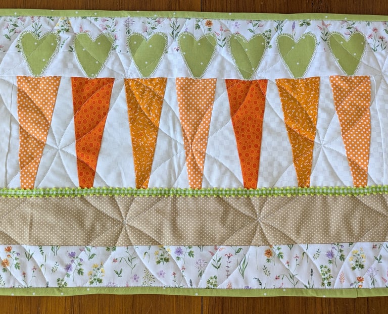 Quilted table runner with heart-topped carrots, floral border, and spring-themed stitching details.