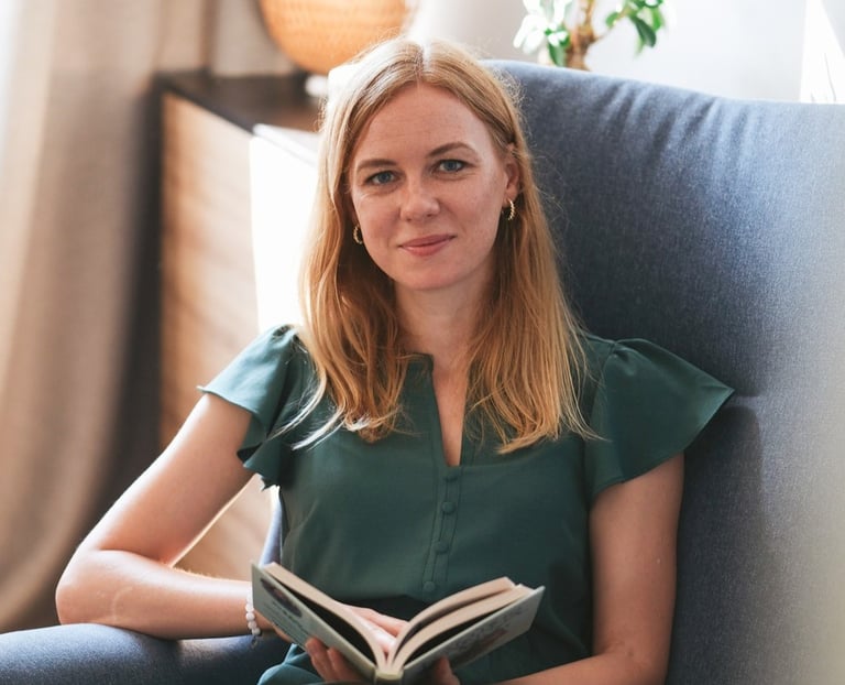 Psichologė Ieva Aukštuolytė sėdinti su knyga krėsle, šviesiame kambaryje..