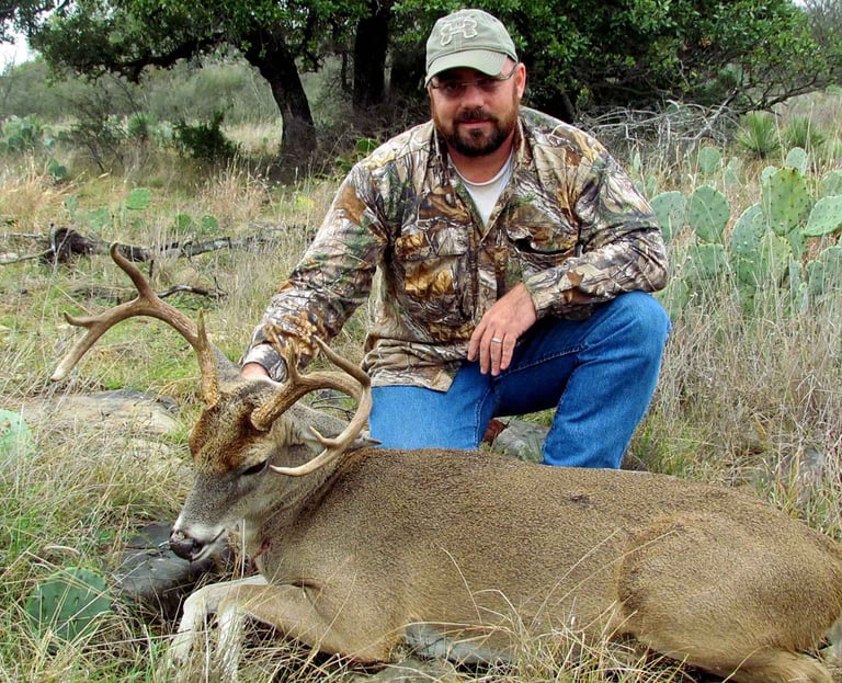 A hunter posing with a trophy whitetail buck in the rugged Texas Hill Country terrain near prickly pear cactus.