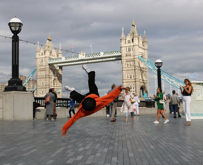YoYo breakdancing with Tower Bridge, London, in the background as passers-by watch.