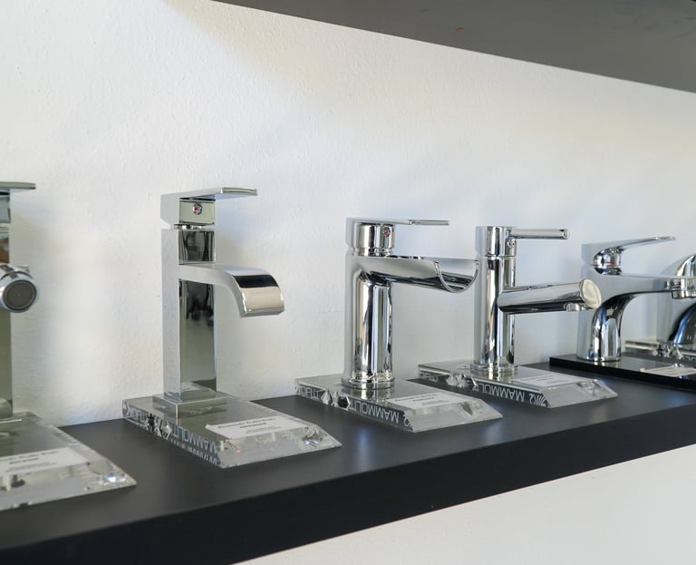 A row of modern polished chrome bathroom sink faucets displayed on a black shelf in a showroom.