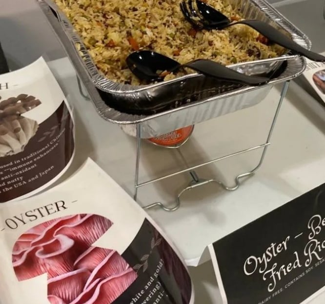 A buffet tray of oyster mushroom fried rice served with black serving spoons at a catered event.