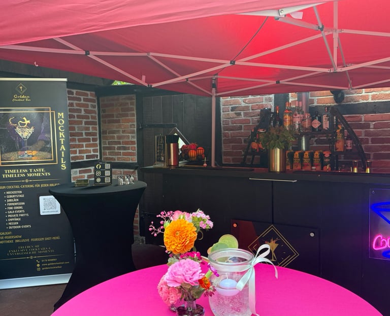 Professional outdoor mobile cocktail bar setup under a red canopy with floral decorations and a drinks menu.