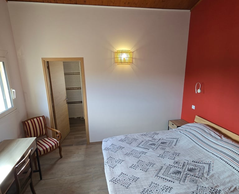 Vue de la chambre d'hôtes depuis la porte d'entrée, avec lit double, bureau et chaise.